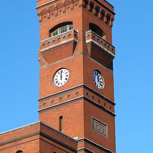 Brick clock tower with a set of 2 60-inch diameter inset tower clocks. This Romanesque style Brick building houses the US Forestry Services , it is known as the Sidney Yates Building, and is located in Washington DC. The 2 clocks are a set of 3, Roman Style clocks. Background of blue sky.