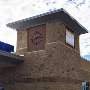 Clock Tower with a 72-inch diameter Marker-style or skeletal style Clock, in a modern style with black powdercoat-finish hour markers, and straight tapered hands.  On a brown and tan brick tower fascia.  This clock is located at St. David's FSED.